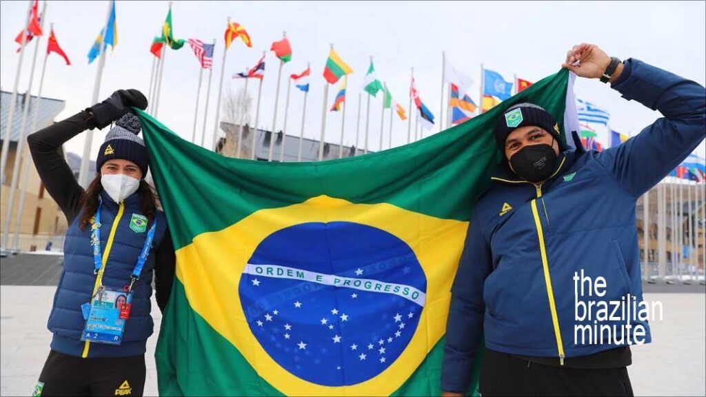 A female and a male wearing winter jackets holding a Brazilian flag.